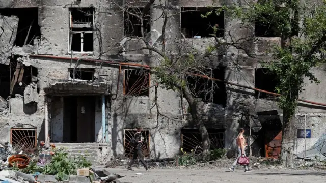 People walk past a residential building heavily damaged during Ukraine-Russia conflict in the southern port city of Mariupol, Ukraine