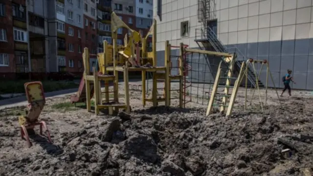 A woman walks past a kids' playground damaged during a shelling in the town of Lysychansk