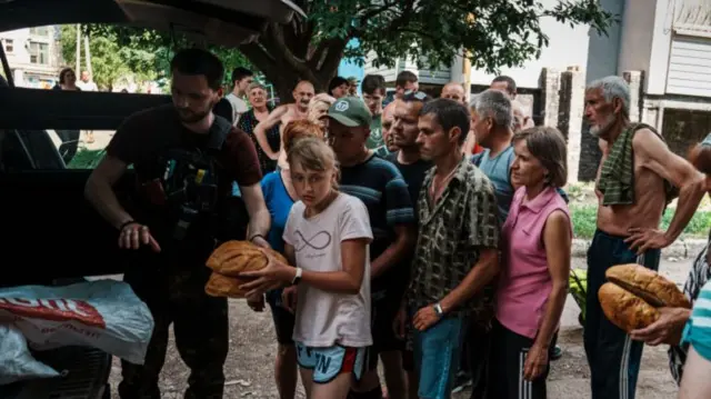 Residents queue to receive bread given out by police officers in the city on 11 June 2022