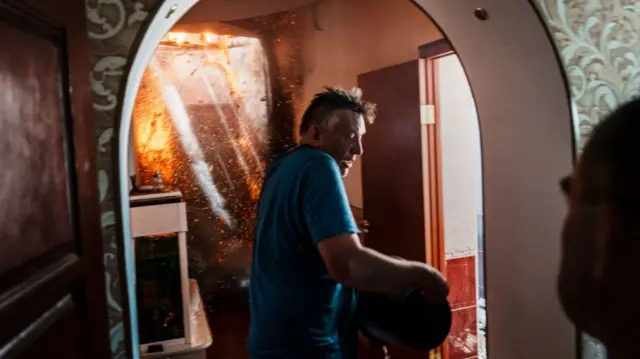 A man tries to put out a fire with a bucket of water, after a bombardment destroyed the home next door in Lysychansk, 11 June 2022