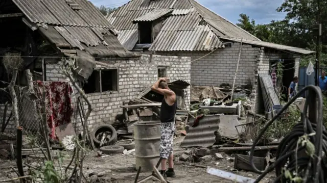 Maksym Katerin stands in the yard of his damaged house after his mother and his step father were killed during shelling