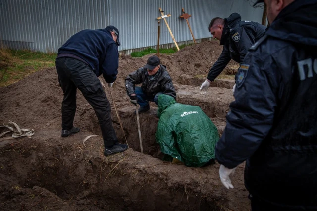 A Bucha resident who buried his neighbours during the occupation helps to bring them up from makeshift graves in April