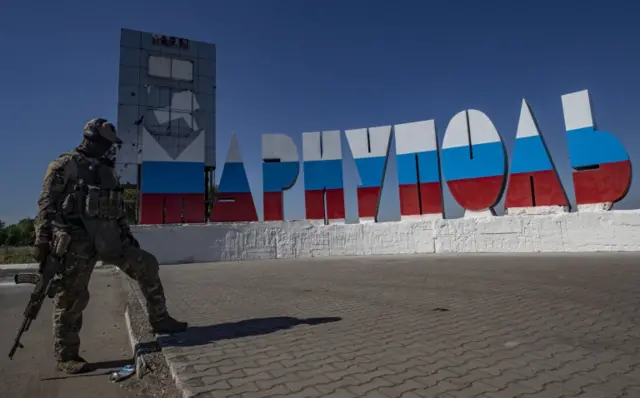 A Russian serviceman stands in front of the Mariupol city sign, repainted in the colours of the Russian flag