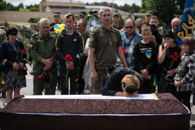 Yuliia Danylchuk, wife of Mykhailo Tereshchenko, cries over his coffin surrounded by mourners