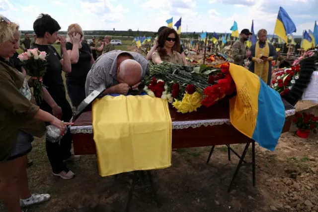 A man weeps on top of Evgeny Khrapko's coffin