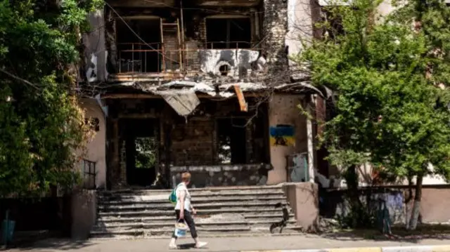 Woman walks past destroyed apartment building in Bucha, Ukraine