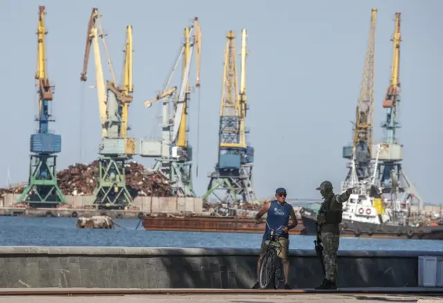 Russian serviceman speaks to a local man as he keeps watch in front of the cargo sea port in downtown of Berdyansk, Ukraine