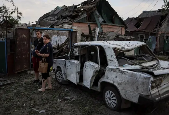 People stand near a building destroyed in eastern Ukraine
