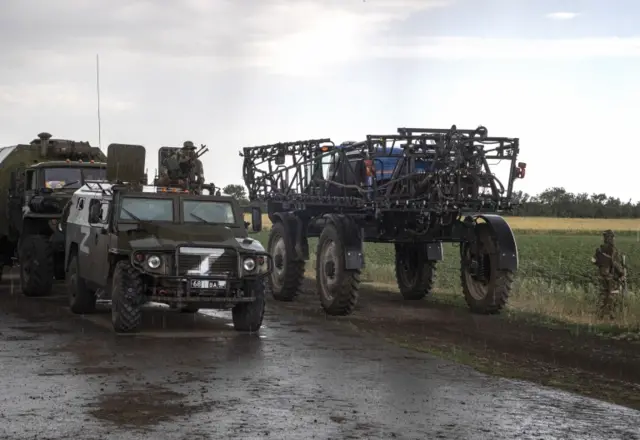 Russian servicemen and their vehicles alongside a tractor and wheat field, near Melitopol