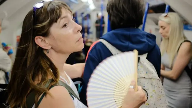 A woman uses a fan to cool down on a tube train in central London