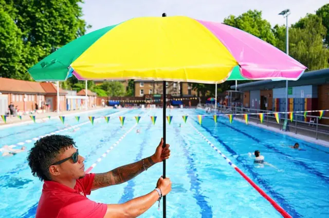 A pool attendant with a parasol at London Fields Lido in Hackney