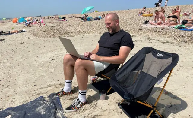 A man checks in on work during his lunch hour while on the beach in Southsea, Hampshire