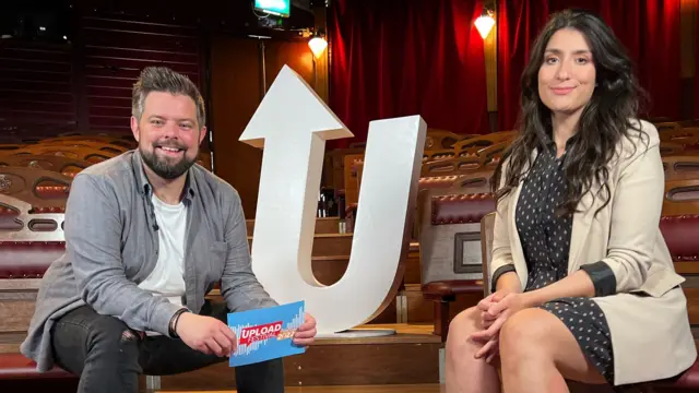 A male presenter and a female comedian sat in the auditorium of a theatre.