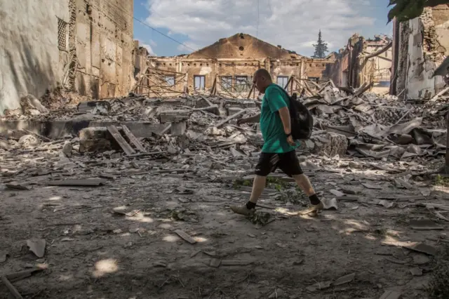 A local resident walks in a front of a building destroyed by a military strik in Lysychansk