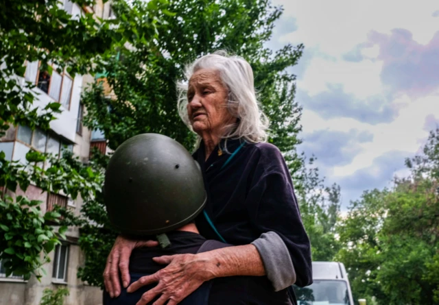 A volunteer carries an old woman to a vehicle to be evacuated from Severodonetsk, eastern Ukraine. Photo: May 2022