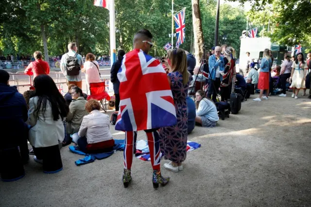 A man wearing a Union Jack suit and high-heeled sparkly boots poses for a selfie