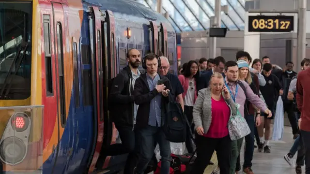 A group of commuters exit a train and walk along a platform at Waterloo station.