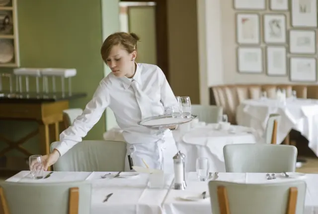 Waitress sets up tables in empty restaurant