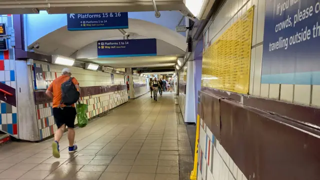 A man in an orange shirt runs through Clapham Junction station