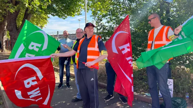 Rail workers hold RMT flags outside Derby station