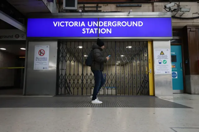 A man walking past the closed gate to a Victoria Underground station entrance in Victoria, London