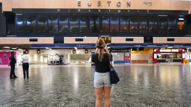 A woman stands in front of the departures board at Euston station