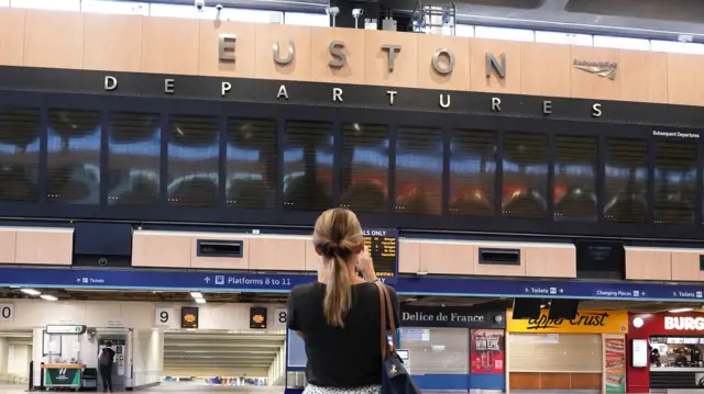 A woman stands in front of a blank departures board at London's Euston station