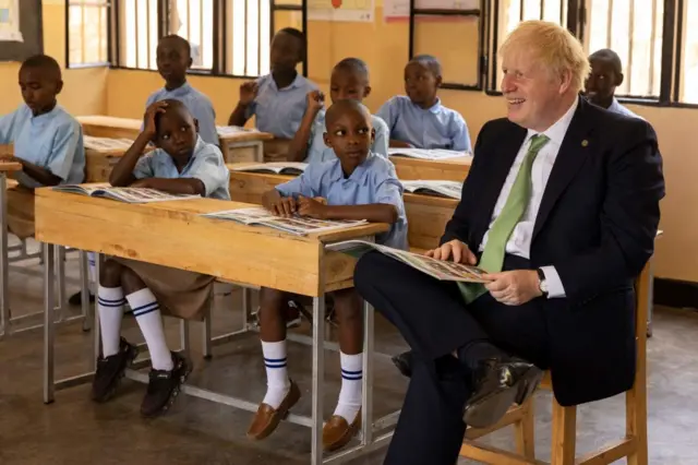 Britain's Prime Minister Boris Johnson (R) interacts with school children as they take part in a lesson during a visit to The GS Kacyiru II School in Kigali on 23 June 2022