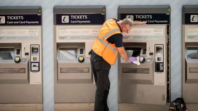 A station worker cleans a ticket machine