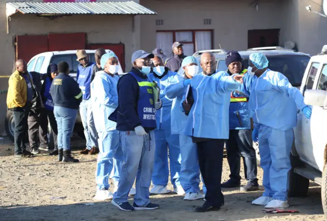 Police and investigators put on protective clothing before going into a township pub in South Africa's southern city of East London