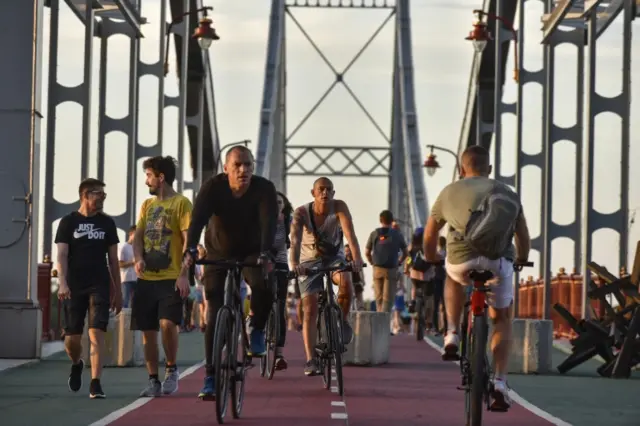 People cycle across a pedestrian bridge over Dnipro River in Kyiv