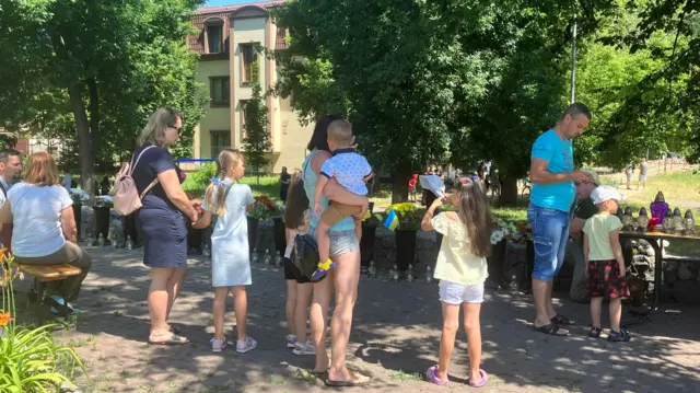 Ukrainian men, women and children gather at the memorial of the Amstor shopping centre in Kremenchuk, central Ukraine