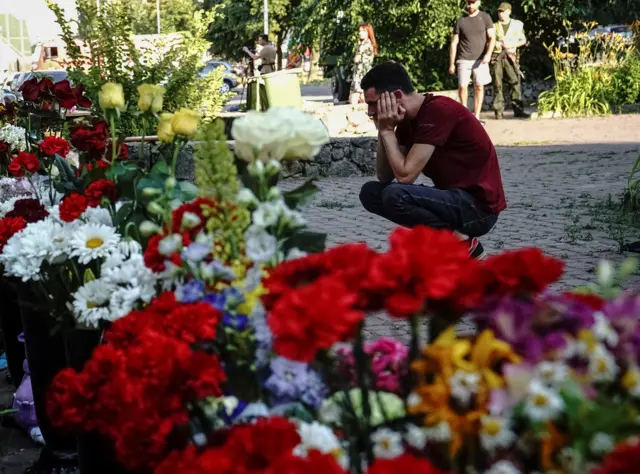 A man reacts near flowers to commemorate victims of a shopping mall hit by a Russian missile strike, in Kremenchuk