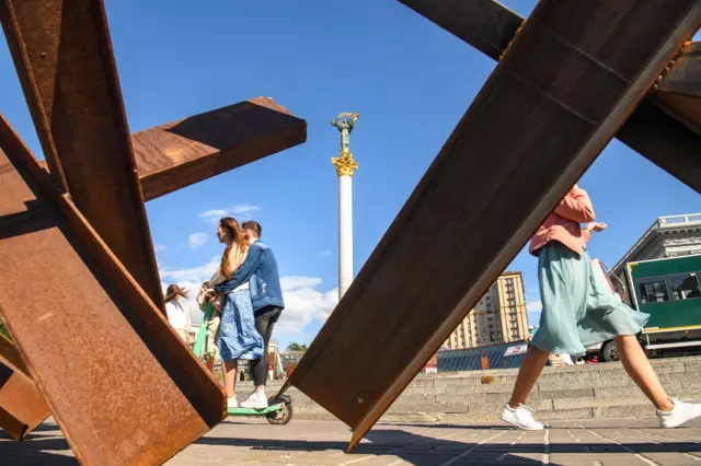 People pass close to anti-tank obstacle defense at the Independence Square in downtown Kyiv, Ukraine, May 24, 2022