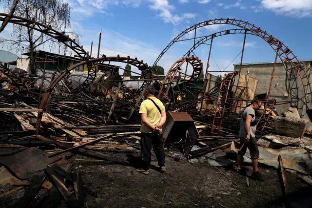 Men look at the remains of a wood warehouse after a strike in Kharkiv