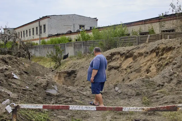 A local man looks on a shelling hole after a recent rocket attack on a wood factory on the outskirts of the small city of Bezlyudovka in the Kharkiv area