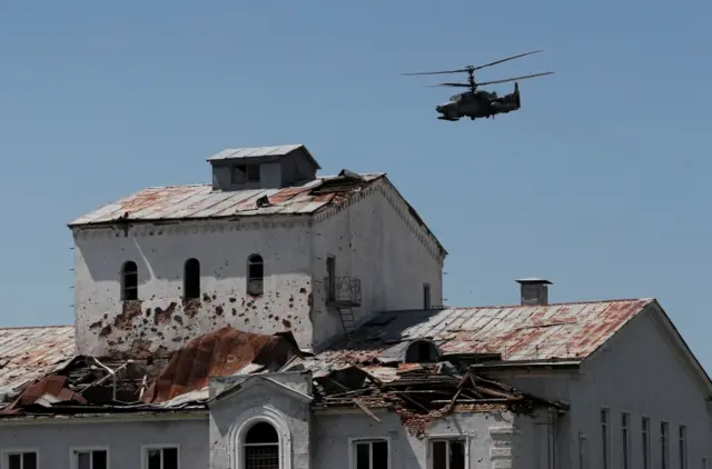 A Russian Ka-52 Alligator attack helicopter flies near a heavily damaged building in Popasna, Luhansk