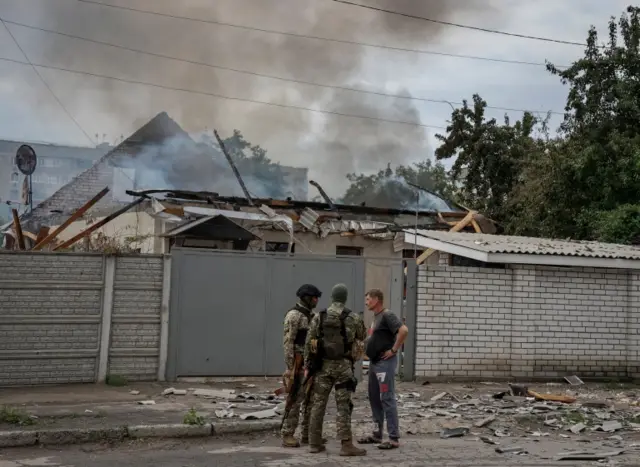 Ukrainian soldiers speak to a man outside is burning home following shelling in Lysychansk, in the Luhansk region