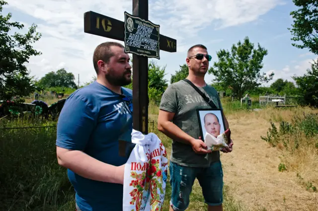 Two men stand holding a cross and a picture