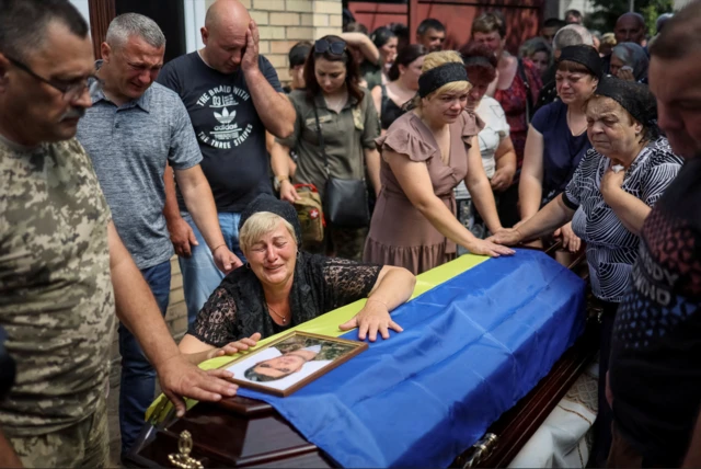 A woman cries on a coffin draped in the Ukrainian flag