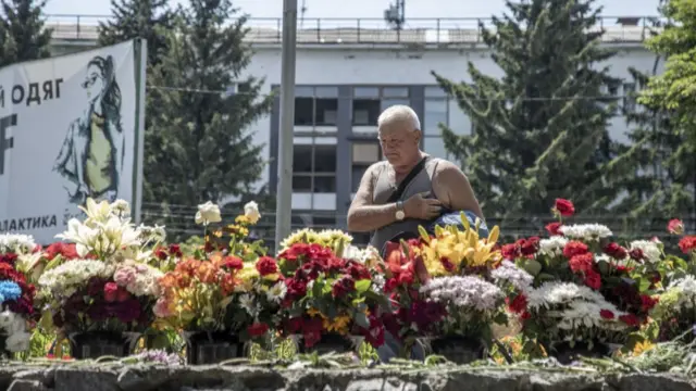 A man mourns in front of row of flowers offered to victims near a shopping centre targeted by a missile strike in Kremenchuk, Ukraine