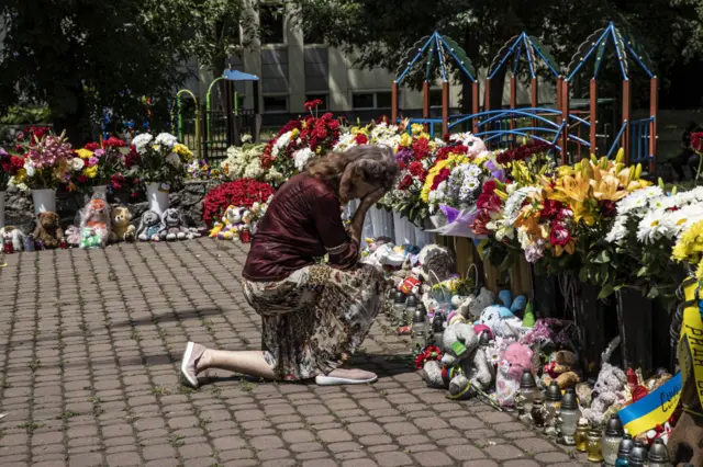 A woman mourns in front of a memorial made of flowers offered to the civilian victims nearby a shopping mall targeted by a missile strike in Kremenchuk