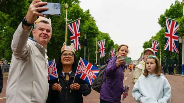 A group of people pose for selfies on the Mall in front of Buckingham Palace