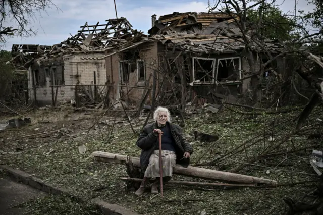 An eldery woman sits in front of destroyed houses after a missile strike, which killed an old woman, in the city of Druzhkivka (also written Druzhkovka) in the eastern Ukrainian region of Donbas on June 5, 2022.