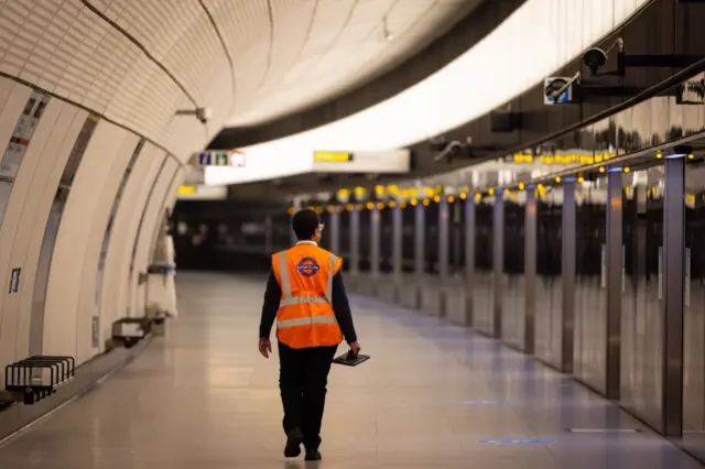 A member of TfL staff walks down an empty platform