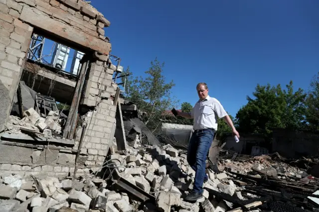 A man walks through rubble by a damaged building