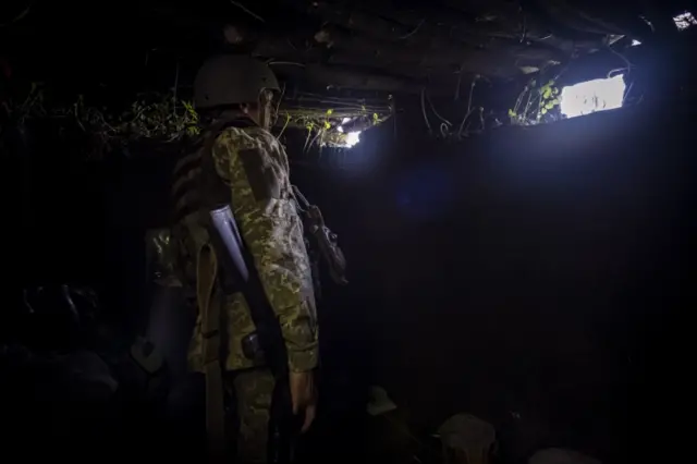 A Ukrainian serviceman keeps watch at a trench position near the frontlines of Izyum