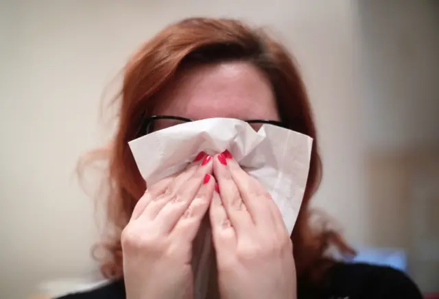 A woman with a cold blowing her nose with a tissue,