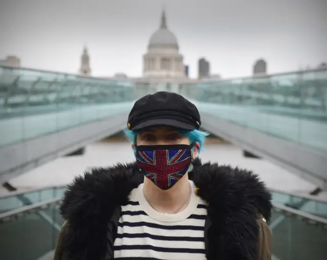 A woman wears a mask with a union jack design at the foot of the Millennium Bridge