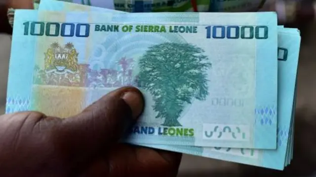 A money changer holds a bundle of Sierra Leone currency notes on a pavement in Freetown - 2018